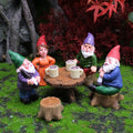 Miniature garden gnomes around a table with coffee cups, set against a natural background.