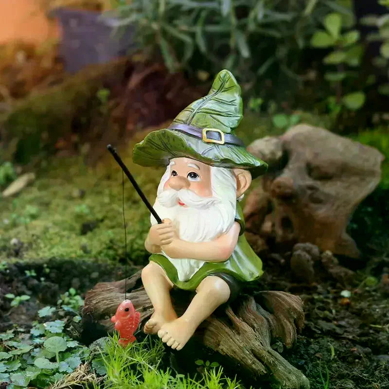 A small garden gnome figurine sitting on a log, holding a fishing rod with a red fish. The gnome has a white beard, a green hat and cloak, and is posed outdoors on a log with a blurred natural background.