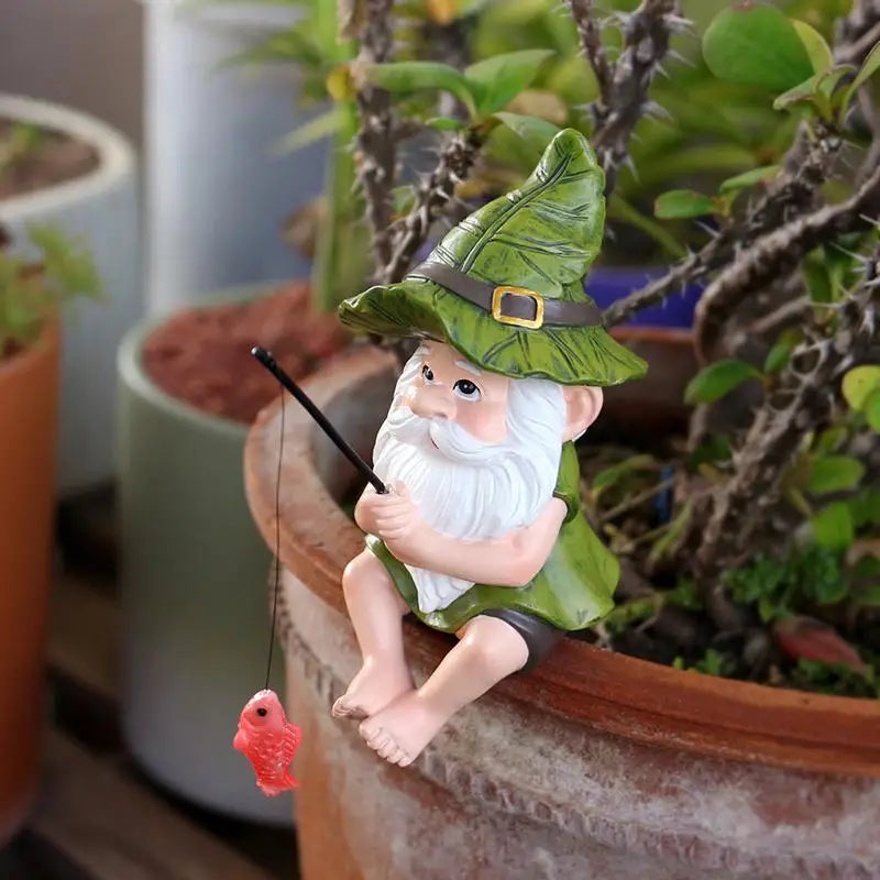 A small gnome garden figurine sitting on the edge of a terracotta planter, holding a fishing rod with a red fish dangling below. The gnome has a white beard, green hat and clothing, and is photographed among potted plants.