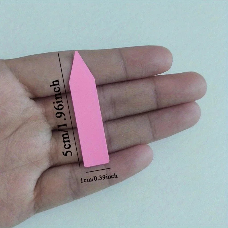 Pink wedge-shaped object held between fingers with measurements on a light background