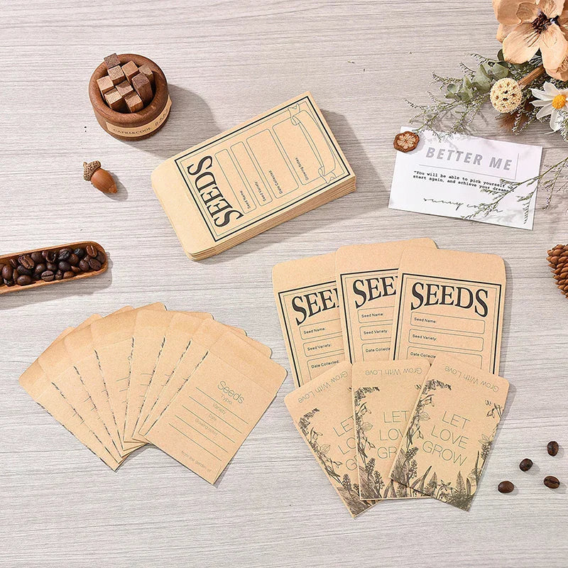 A styled flat-lay of coffee seed packets and a matching envelope on a light wood surface, surrounded by coffee beans, a small wooden box, dried flowers, and a card reading 'BETTER ME'. The packets are kraft paper with black printed text including 'SEEDS' and 'LET LOVE GROW'.